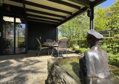 Terras met tuinstoelen en bronzen tuinbeeld bij vakantiehuis De Kateeker Ootmarsum