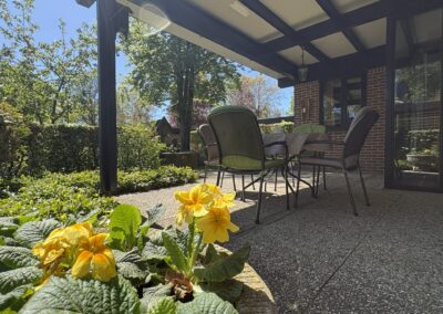 Terrashoek met stoelen en gele bloemen onder overkapping bij bungalow De Kateeker Ootmarsum