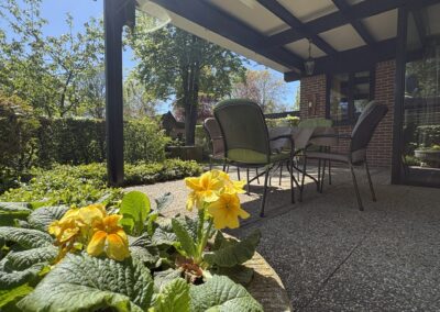 Terras met stoelen en bloeiende gele bloemen bij vakantiehuis De Kateeker Ootmarsum