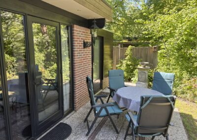 Terras met blauwe tuinstoelen en tafel naast de schuifpui van bungalow De Kateeker Ootmarsum
