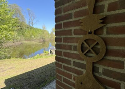 Detail bakstenen muur van vakantiehuis De Kateeker met decoratief houtstuk en Kleikoel op achtergrond